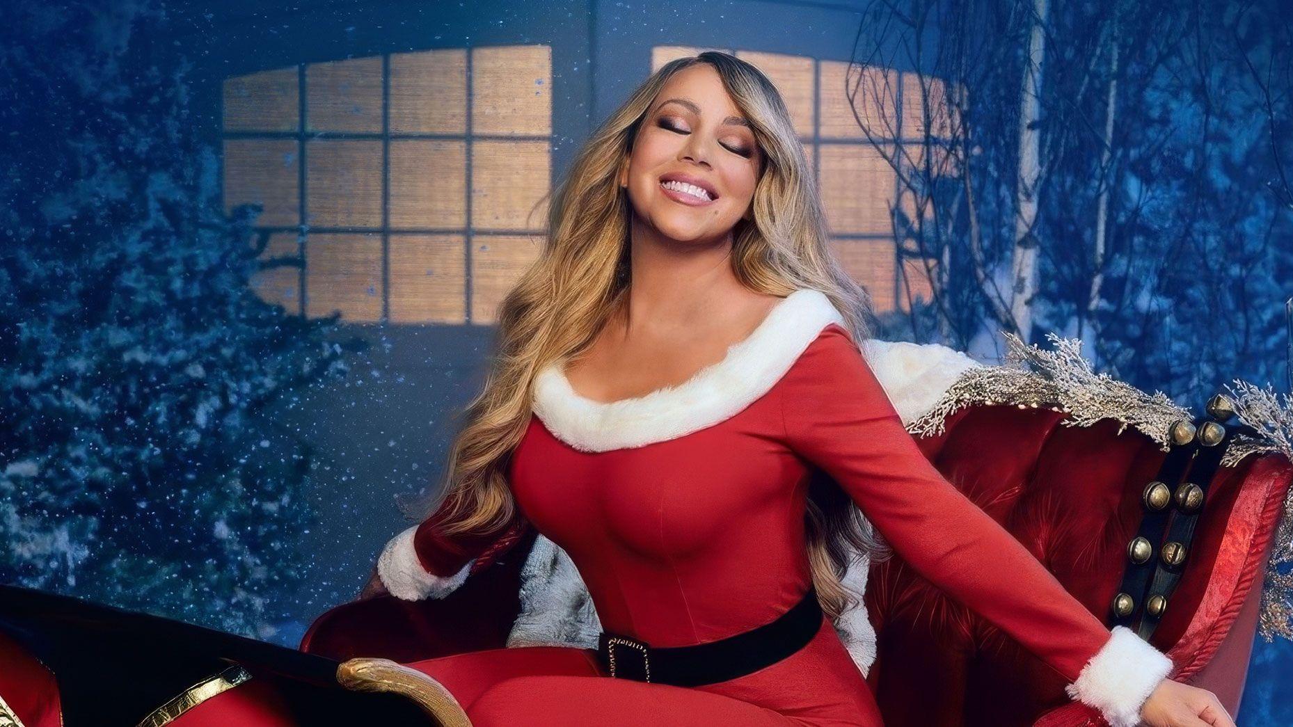 Mariah Carey in a red Santa outfit on a sleigh in a snowy night scene.